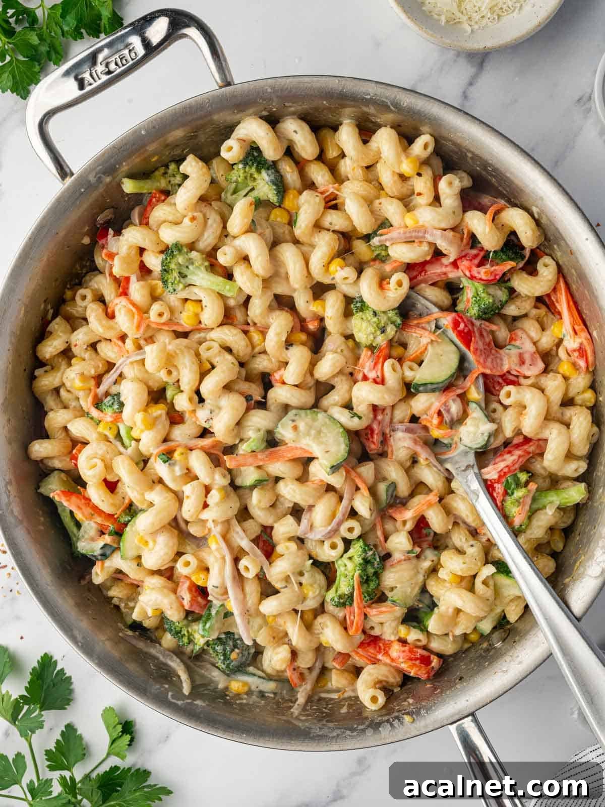 A spoon serves cheesy pasta with vegetable from a skillet.
