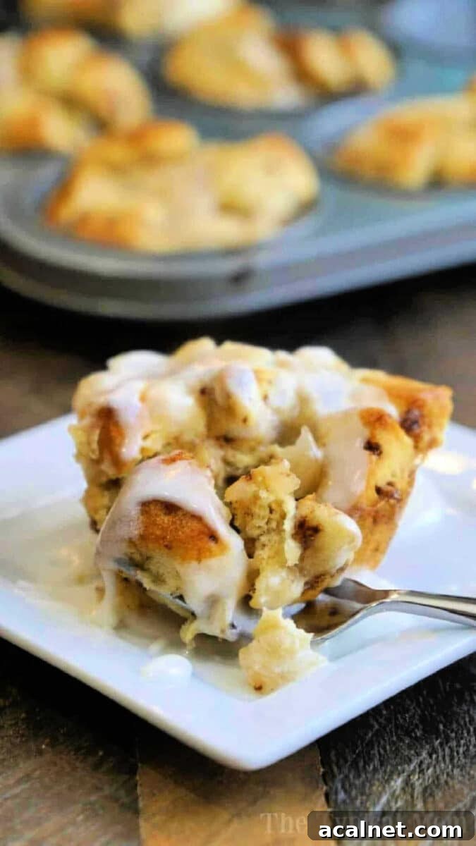 A gooey cinnamon roll muffin with icing on a white plate, with more monkey bread muffins in a tray in the background.