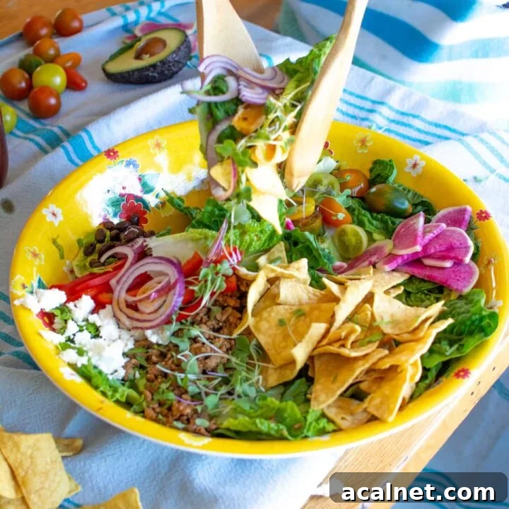 A woman tossing a taco salad sitting at a wood table.