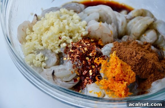 Glass bowl containing shrimp, minced garlic, chili flakes and spices
