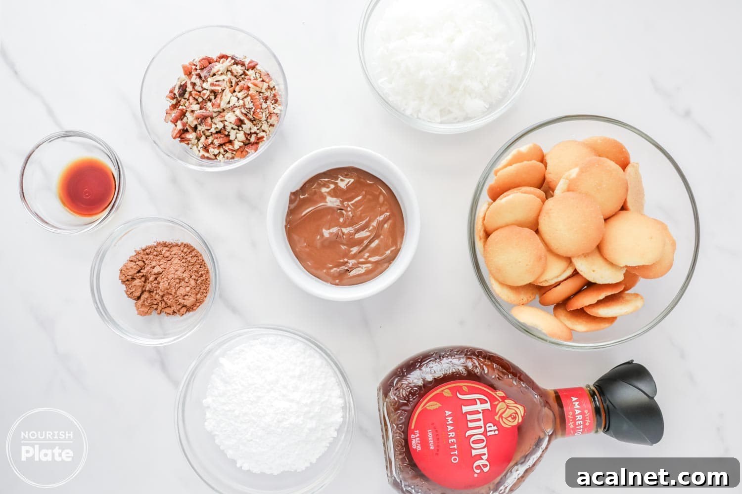 Amaretto Booze Balls: Almond Liqueur Truffles Recipe 3 Overhead view of Amaretto ball ingredients arranged in glass bowls on a white surface, including vanilla wafers, chopped pecans, shredded coconut, powdered sugar, cocoa powder, Nutella, pure vanilla extract, and a bottle of Amaretto liqueur.