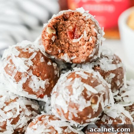Close-up of chocolate Amaretto balls coated in shredded coconut, stacked in a bowl with one ball bitten open to reveal a nutty chocolate interior and a cherry piece inside.