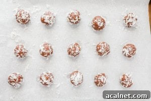 Amaretto Booze Balls: Almond Liqueur Truffles Recipe 8 Chocolate Amaretto balls coated in shredded coconut on a parchment-lined baking sheet.