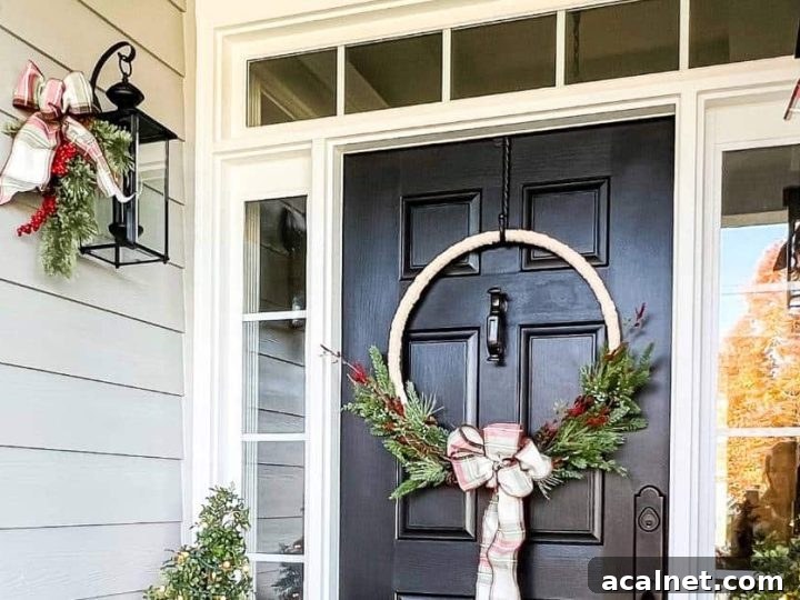 Black front door with transom and sidelights decorated for Christmas with a hoop wreath, greenery, and plaid ribbon.
