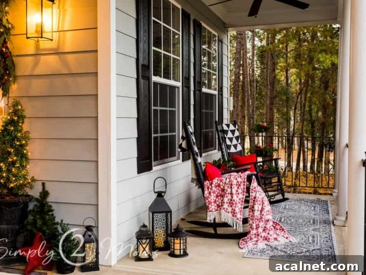 covered front porch with rocking chairs and lanterns decorated for Christmas with red pillows, cozy throw, red woven stars, and twinkle lights