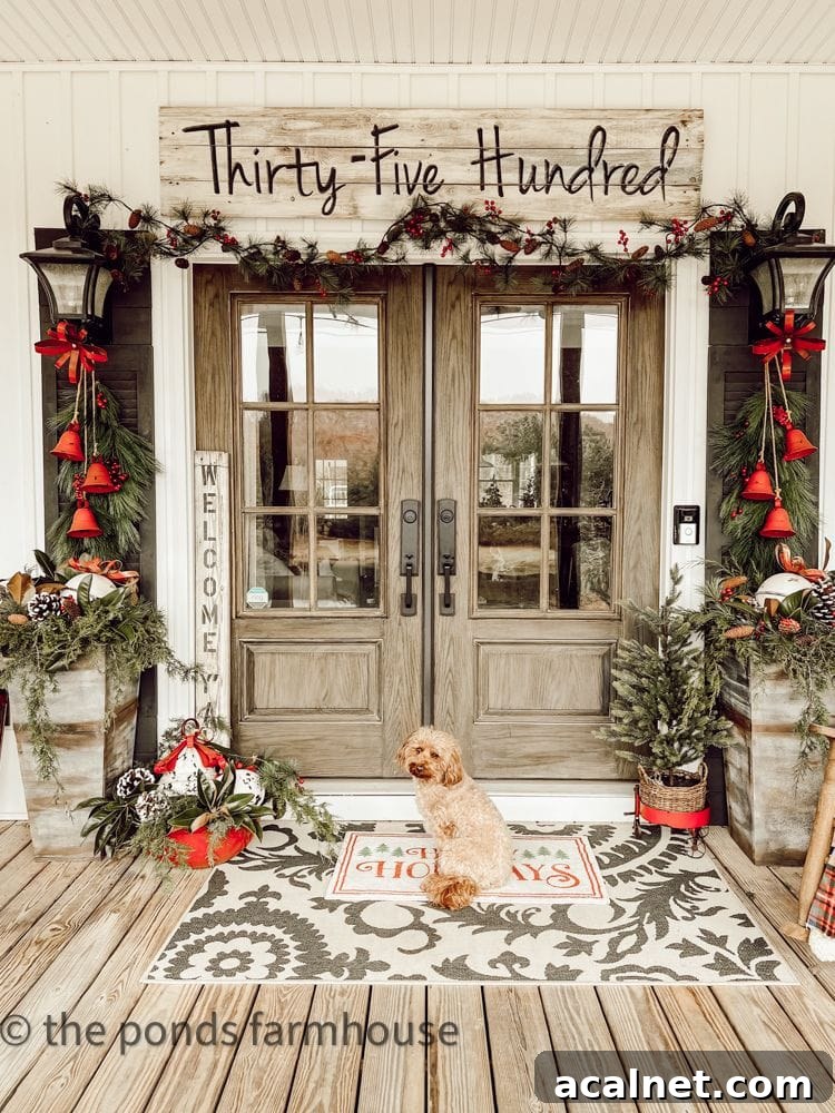 Modern farmhouse front porch with wood double doors decorated for Christmas with greenery and red bells