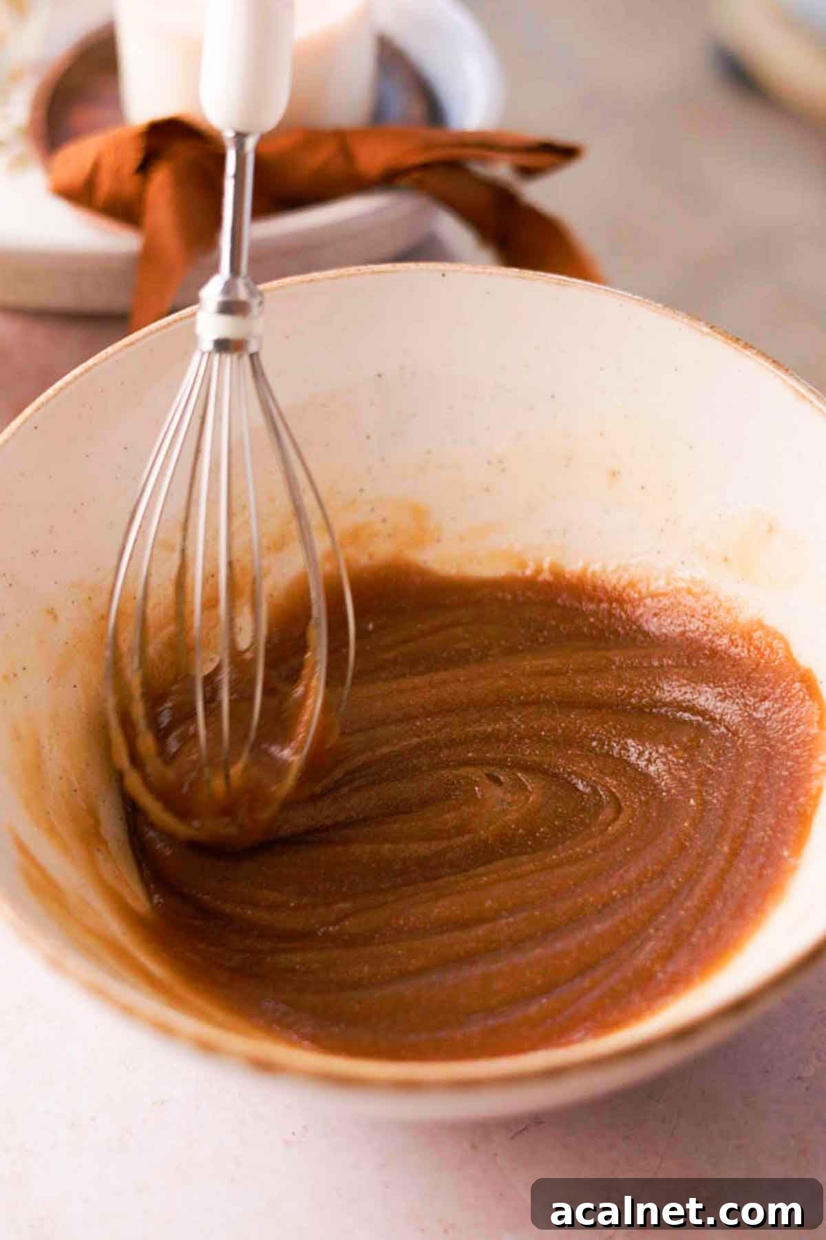 whisking melted butter and sugar inside ceramic bowl with wire whisk