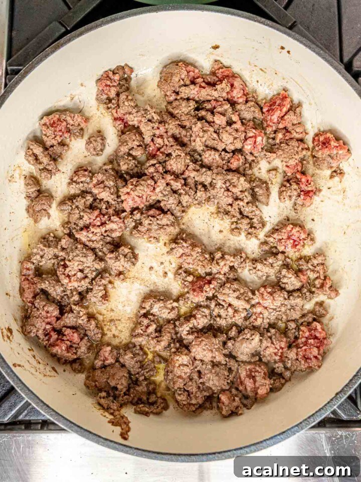 Ground beef browning in a wide skillet until mostly cooked through.