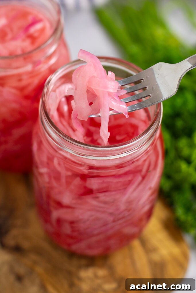 A fork lifting bright pink pickled red onions out of a canning jar.