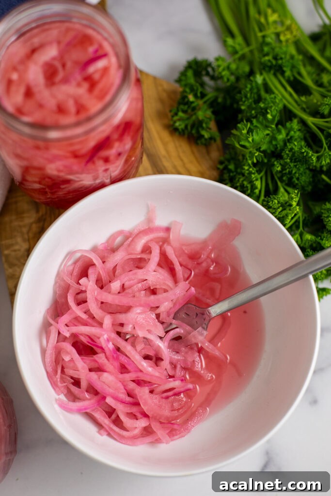Quick pickled red onions in a bowl with a jar of onions and a bunch of fresh parsley behind.