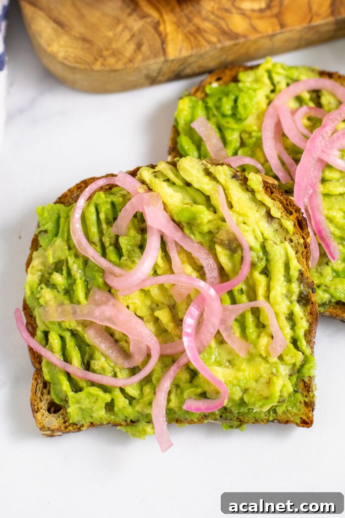 A slice of avocado toast topped with red onions laying on a corner of a second slice.