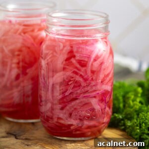 Two mason jars filled with bright pink quick pickled red onions on a small cutting board with a bunch of fresh parsley behind.
