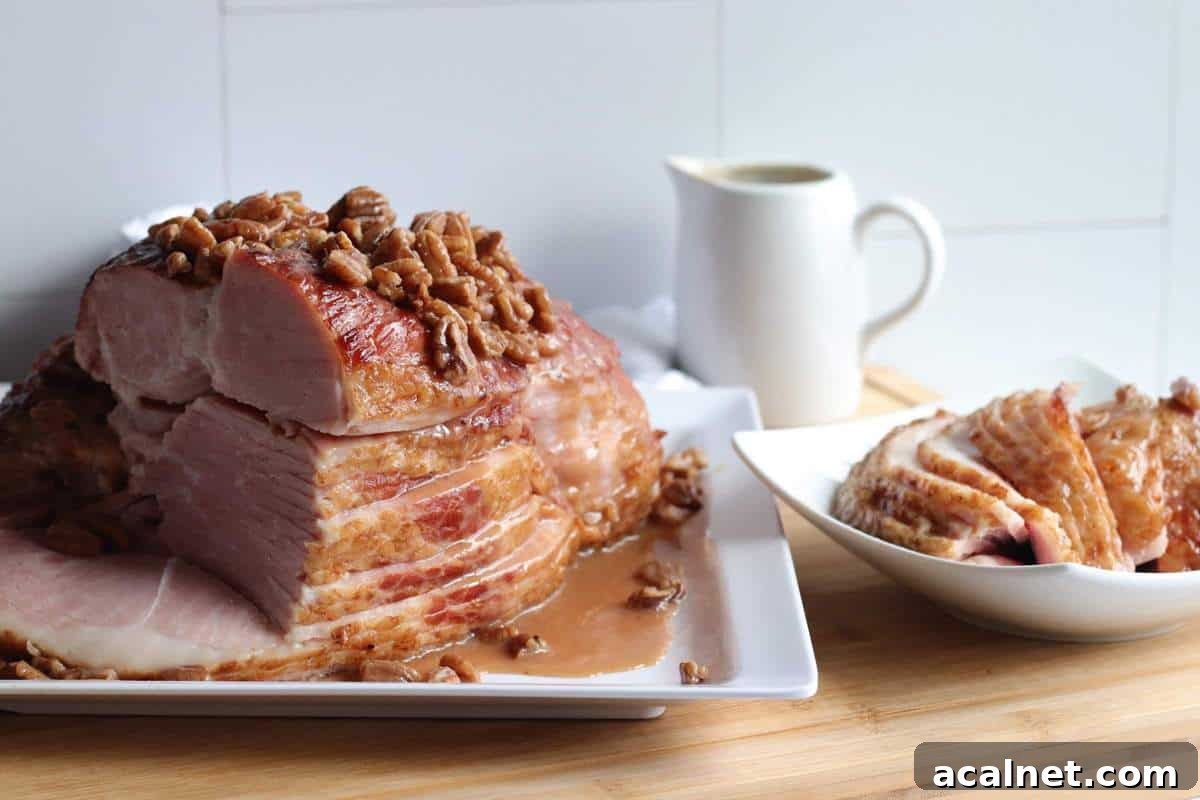 Maple-Glazed Holiday Ham Recipe with Simple Prep and Juicy Results 2 A sliced ham on a white plate with maple, bourbon, and pecan glaze drizzled over the top of it with slices off to the side.
