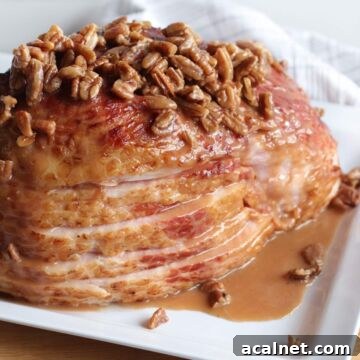 Maple-Glazed Holiday Ham Recipe with Simple Prep and Juicy Results 11 A sliced ham on a white plate with maple, bourbon, and pecan glaze drizzled over the top of it.