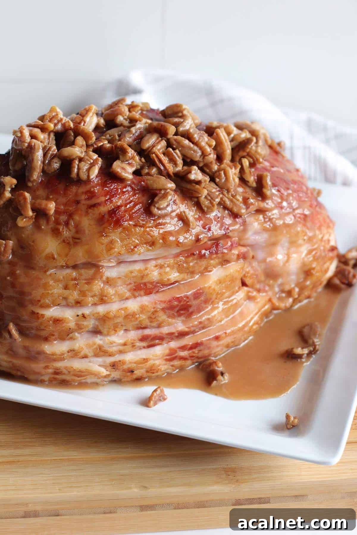 Maple-Glazed Holiday Ham Recipe with Simple Prep and Juicy Results 7 A sliced ham on a white plate with maple, bourbon, and pecan glaze drizzled over the top of it.