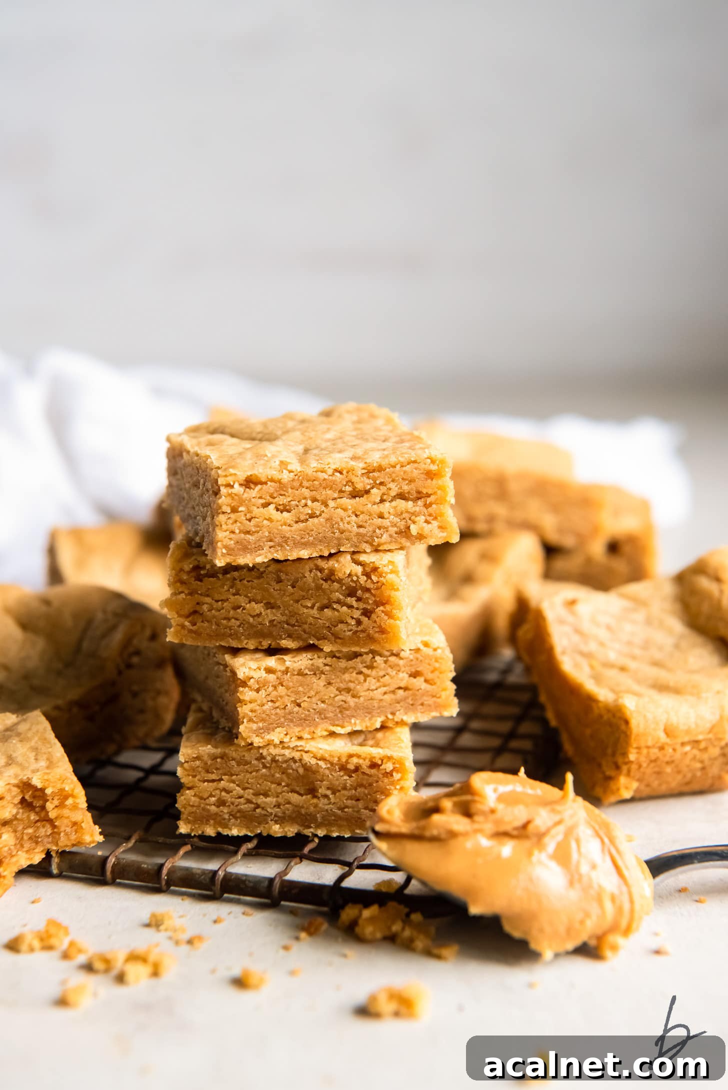 Chewy Peanut Butter Cookie Bar Recipe for Busy Bakers 2 stack of peanut butter cookie bars next to more bars and spoonful of peanut butter.