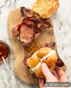 overhead shot of 2 hot cross bun bacon sandwiches with hand holding one on small wooden board