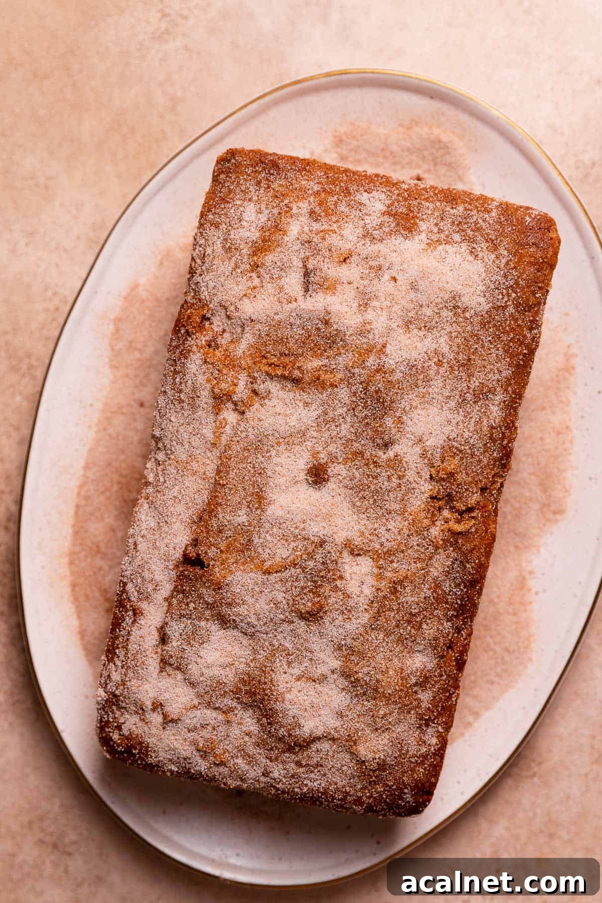 The cinnamon donut cake on a white plate being coated in cinnamon sugar.