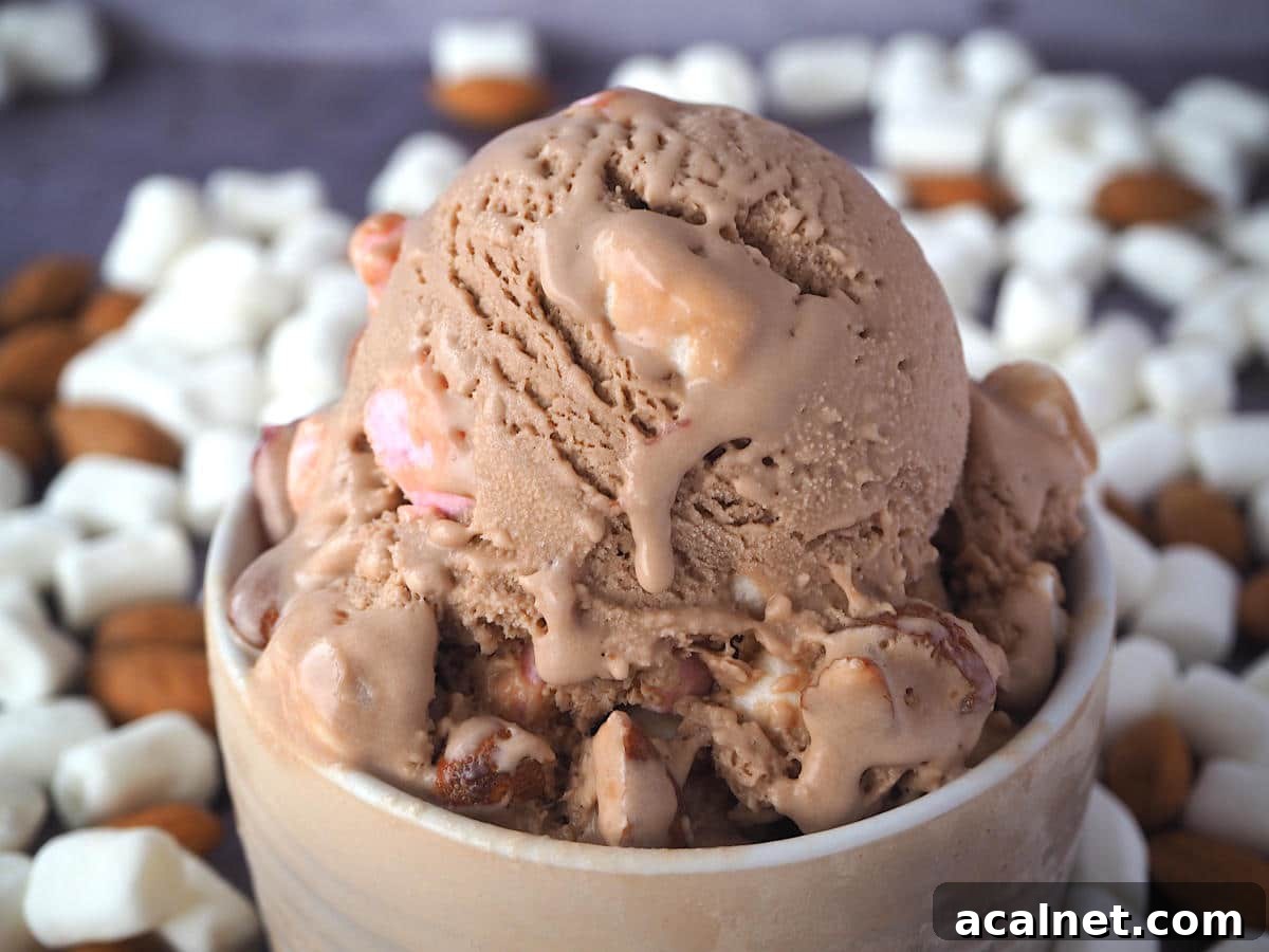 Close up scoop of rocky road ice cream with ice cream drip in a brown bowl, with marshmallows and almonds in the background.