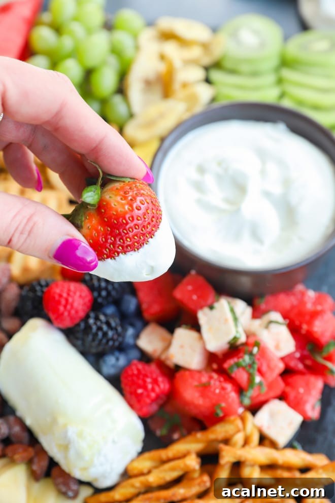Fresh Fruit Charcuterie Board Ideas for Entertaining 9 Dipping a strawberry in whipped cream with hand holding the strawberry picture