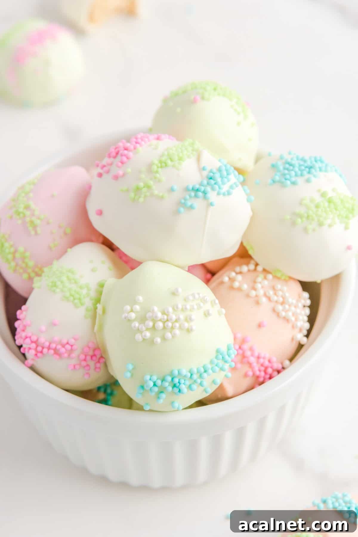 a pile of easter egg truffles in a white bowl on a counter top, with more truffles around it