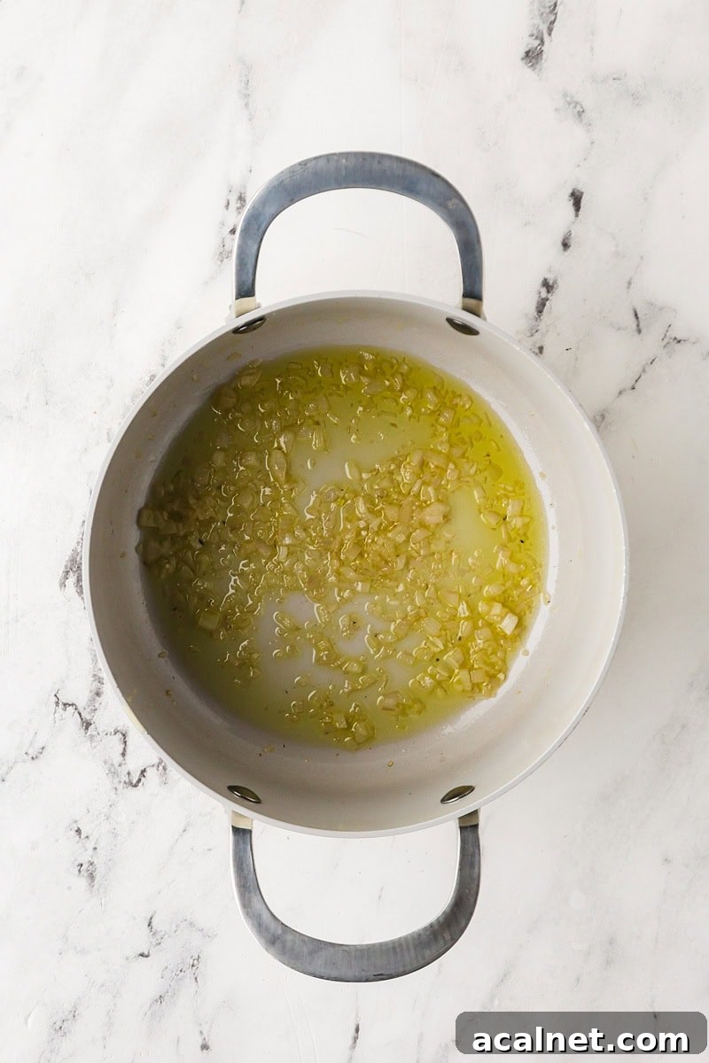 Overhead view of shallot cooking in olive oil in a saucepan.