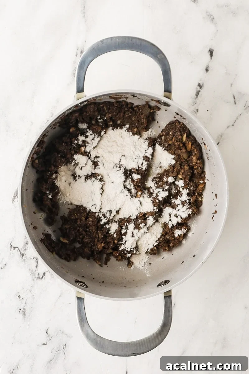 Flour sprinkled over cooked mushrooms in a saucepan.