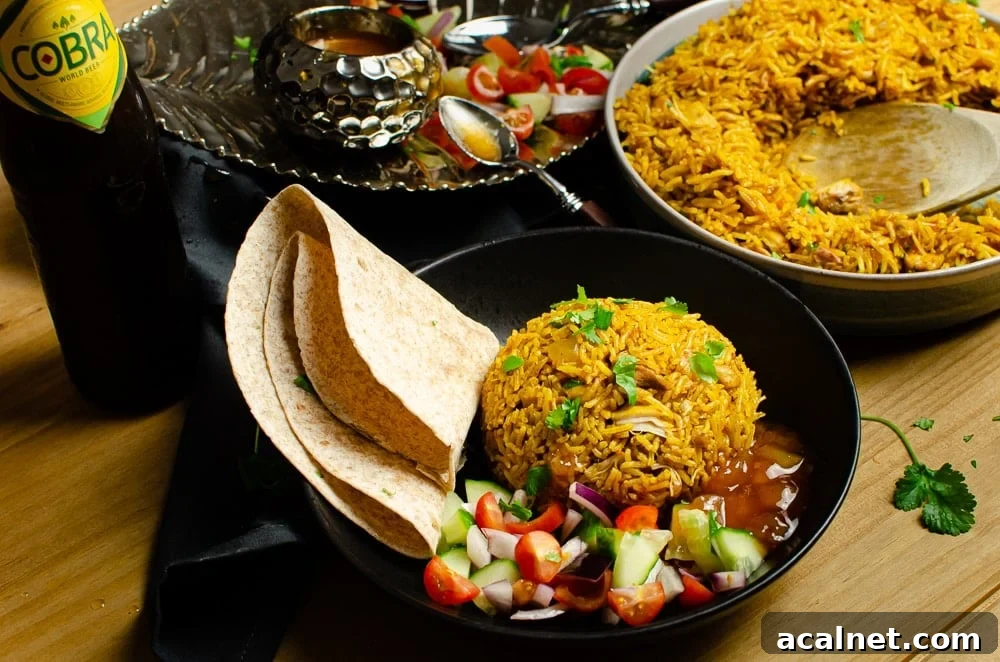 Pressure cooker Chicken Biryani served in a green bowl with chopped coriander on top, salad, mango chutney,Chapati and a bottle of cobra beer served on the side