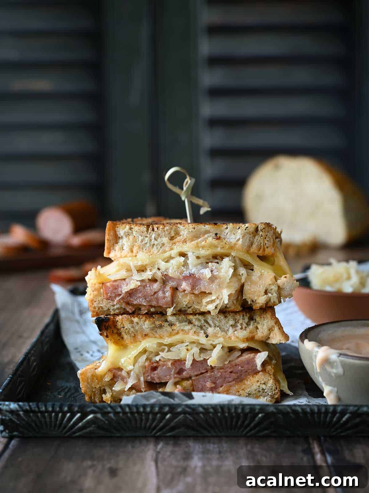 Kielbasa Reuben Sandwich Recipe — Smoky Sausage & Sauerkraut Melt 2 Kielbasa sandwiches stacked on top of each other with condiments on the side.