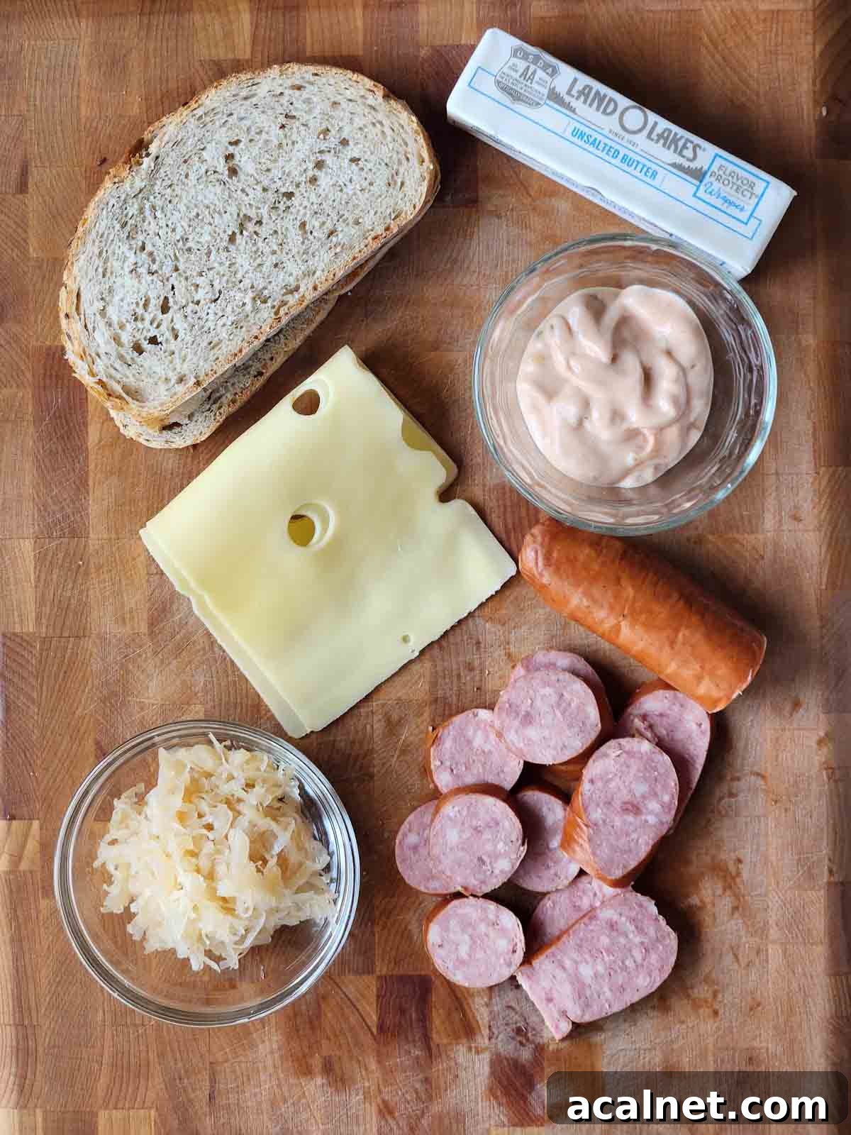 Kielbasa Reuben Sandwich Recipe — Smoky Sausage & Sauerkraut Melt 3 Ingredients for a kielbasa Reuben sandwich on a cutting board.