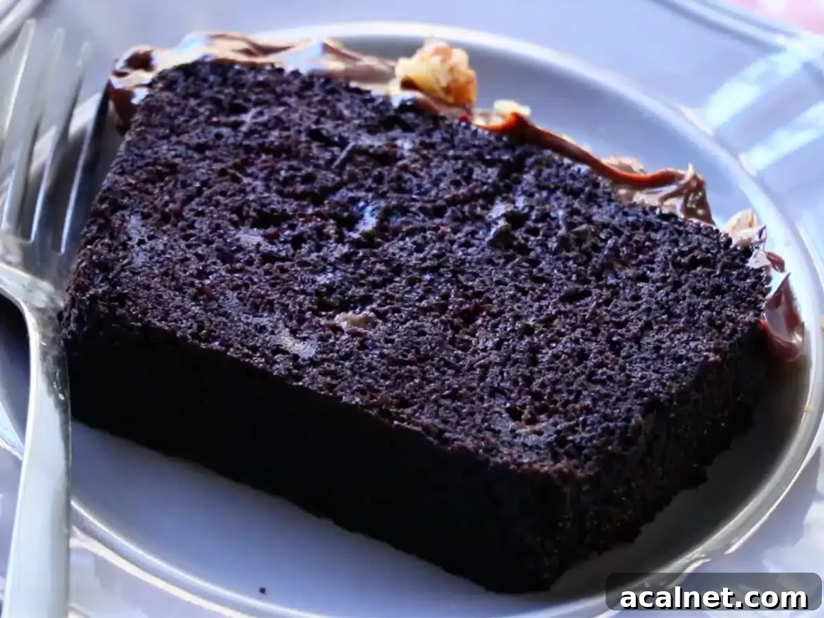 A slice of moist chocolate banana cake, frosted with ganache on a gray plate.
