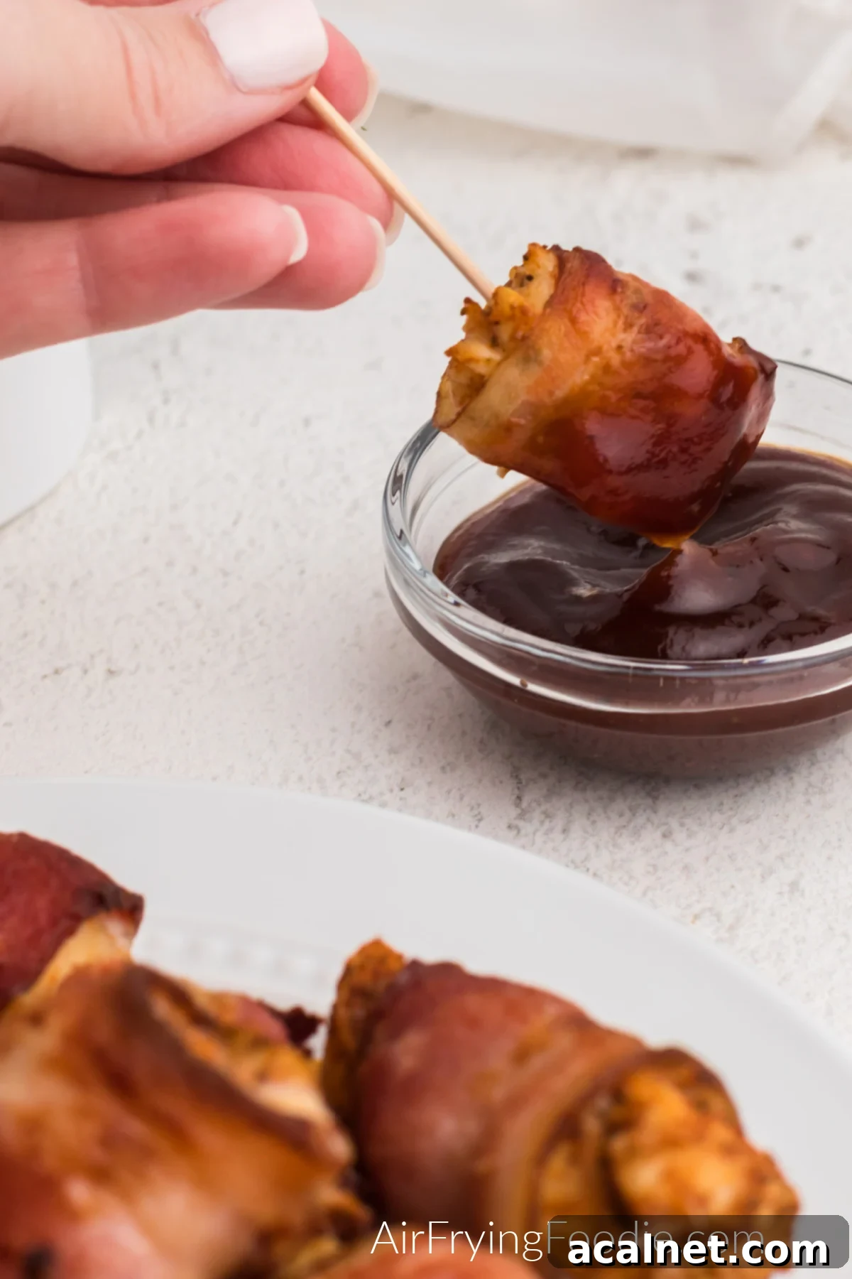 Bacon wrapped chicken bites being dipped in BBQ sauce. 