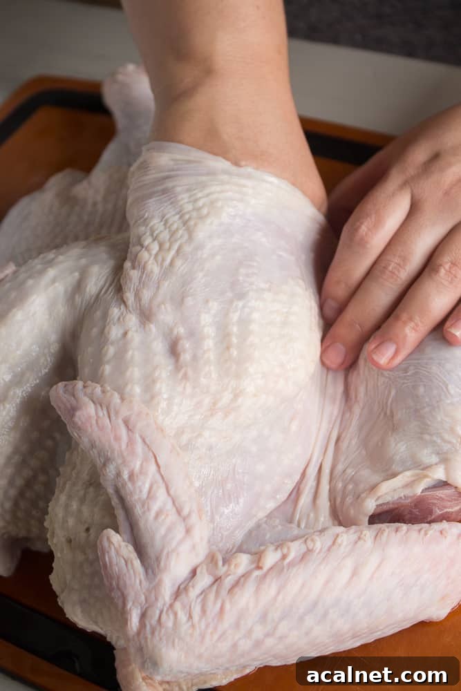 Spatchcocked Whole Turkey Smoked on a Traeger Grill 4 A pair of hands separating the skin from the breast of a raw turkey.