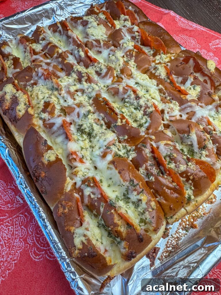 Pepperonis stuffed in Hawaiian rolls coated in melted cheese with garlic butter poured on top and baked until golden brown on a foil lined baking sheet resting on a red napkin.