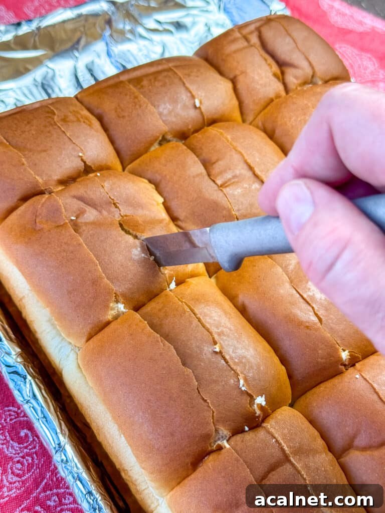Hand holding a knife cutting two rows of slits in the top of Hawaiian rolls.