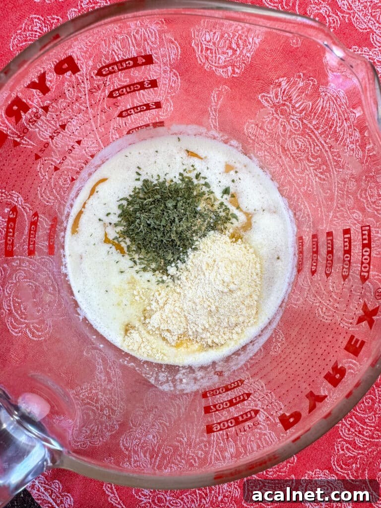 Glass dish with melted butter, Italian seasoning, and grated parmesan cheese on a red and white napkin.