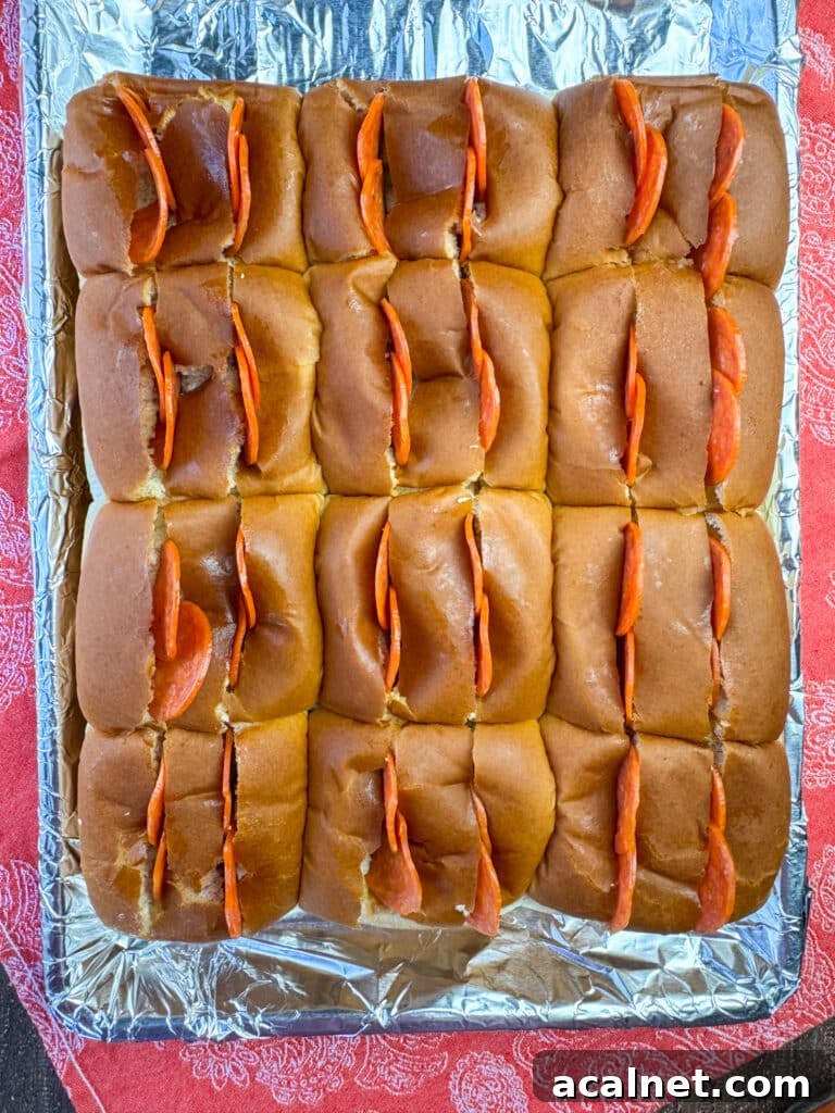 Four pepperonis pushed into partial cuts in the top of dinner rolls on a foil lined sheet.