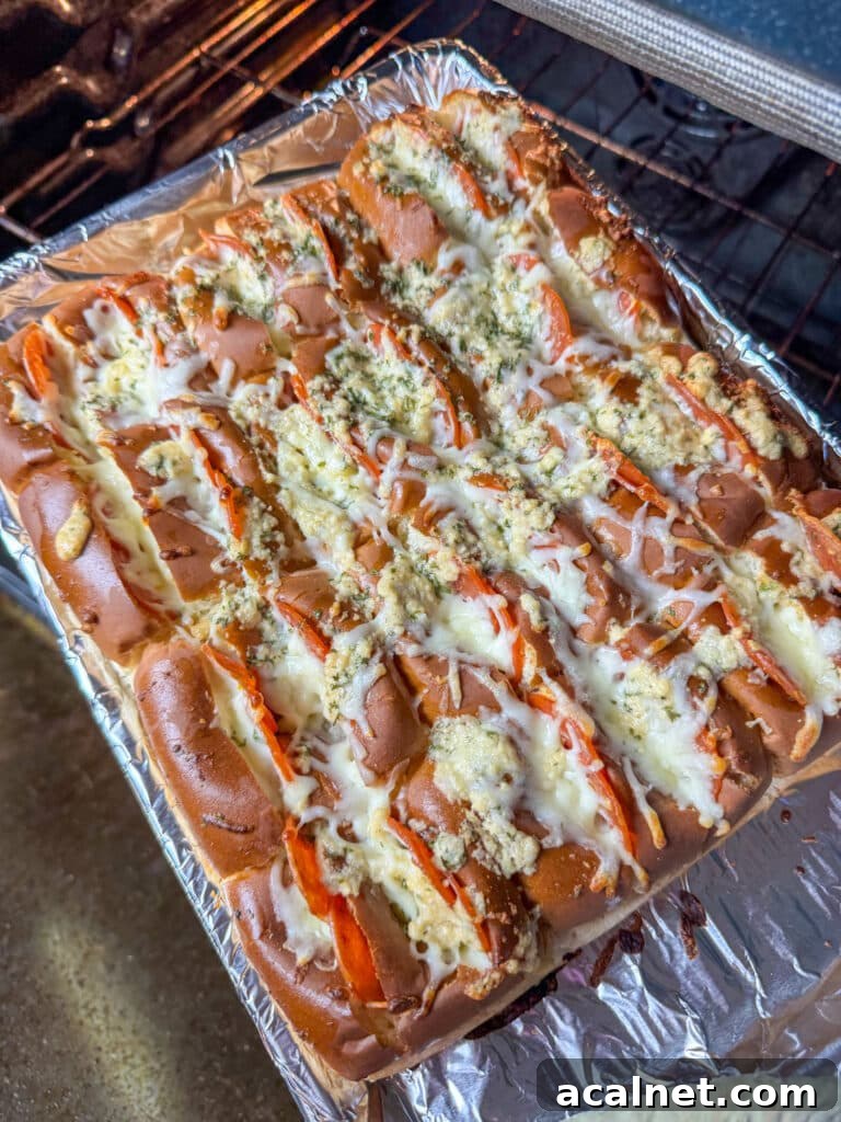 Pull apart pepperoni sliders made with Hawaiian rolls being pulled out of a warm oven with melted cheese and a delicious garlic butter topping.