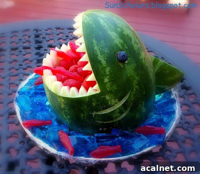 A watermelon carved to resemble a shark's head with Sweedish Fish in its mouth