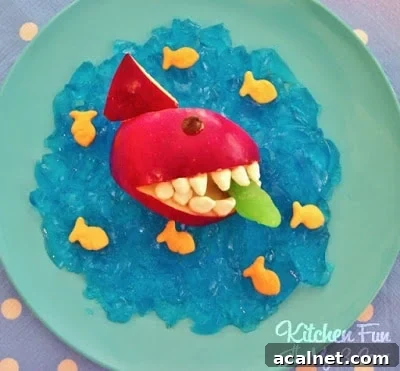 An apple carved and decorated to look like a shark with blue jello resembling water underneath it