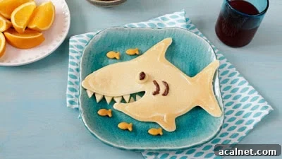 A pancake in the shape of a shark with five goldfish beside it