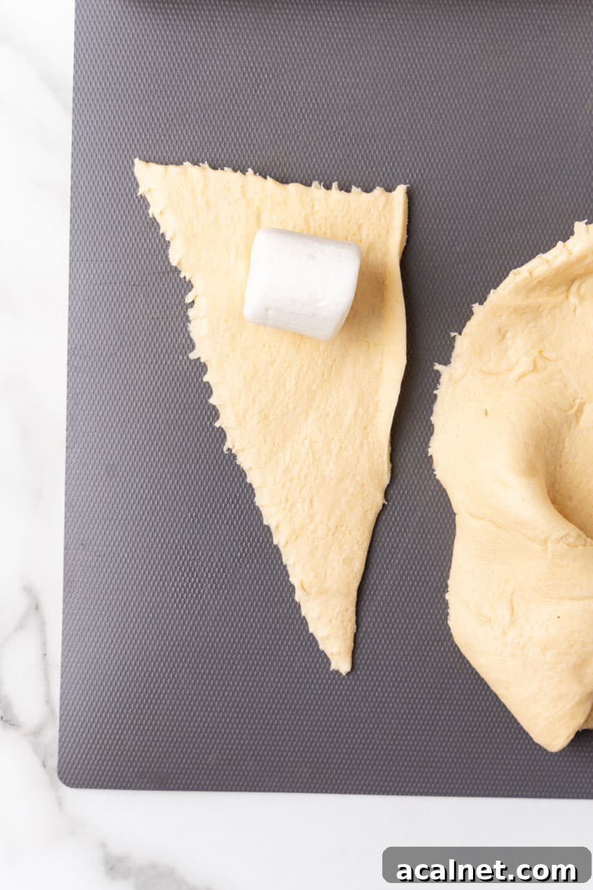 a large marshmallow on a crescent roll triangle on a gray cutting board