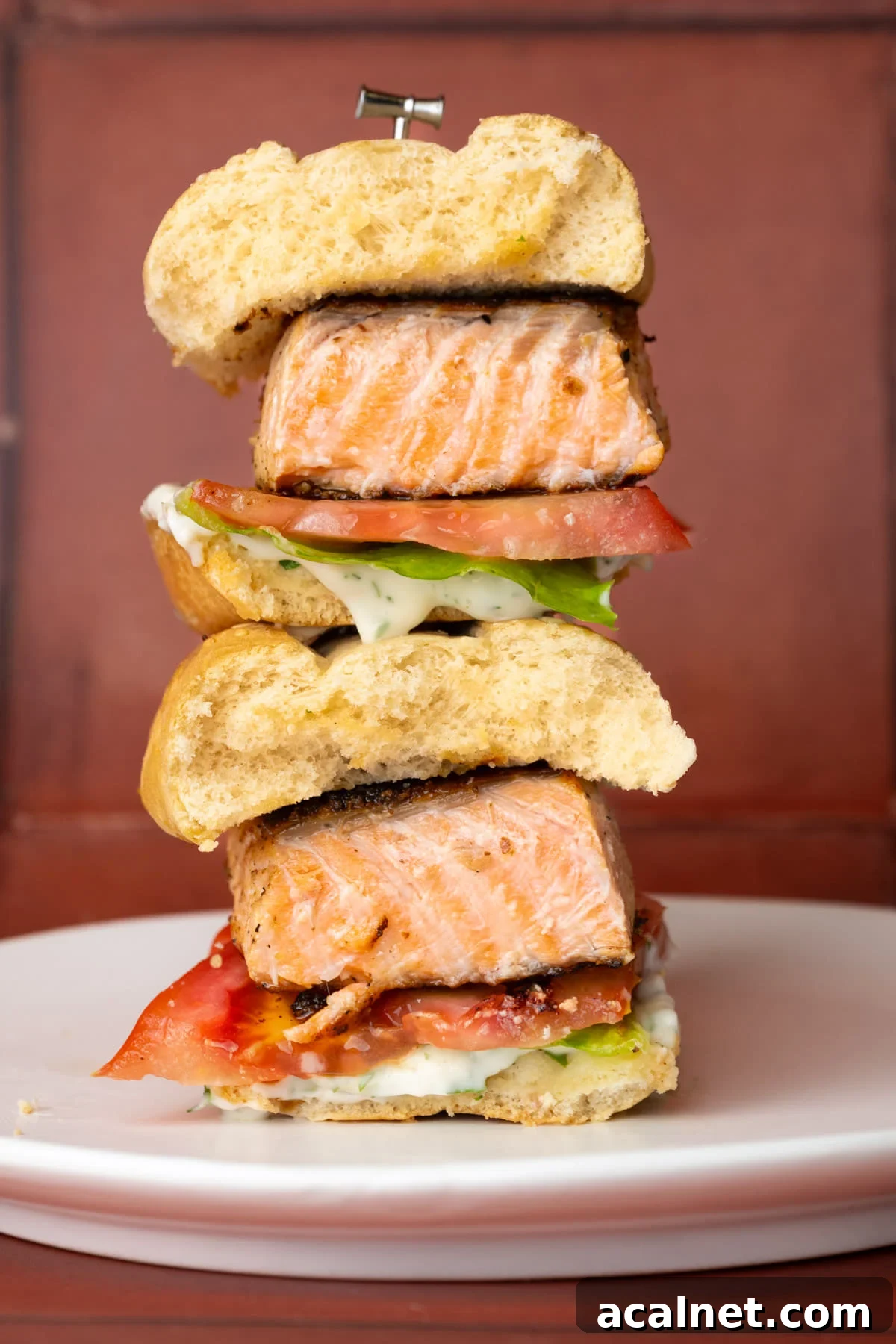 Salmon sandwich with tomato and lettuce sliced in half with halves stacked on top of one another.