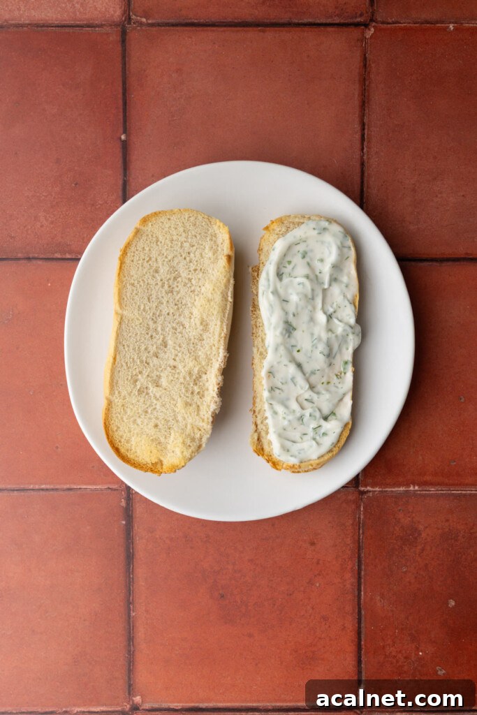 Spreading tartar sauce evenly over bottom bun or a hoagie roll.