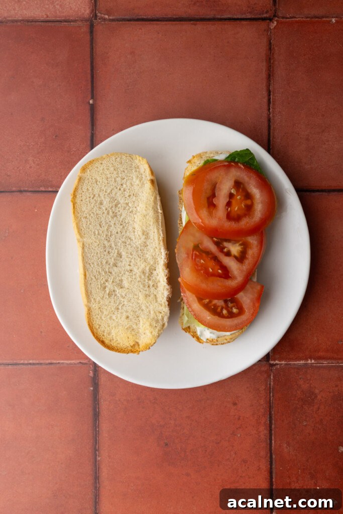 Stacking lettuce and tomato on top of bread with tartar sauce to make a salmon sandwich.
