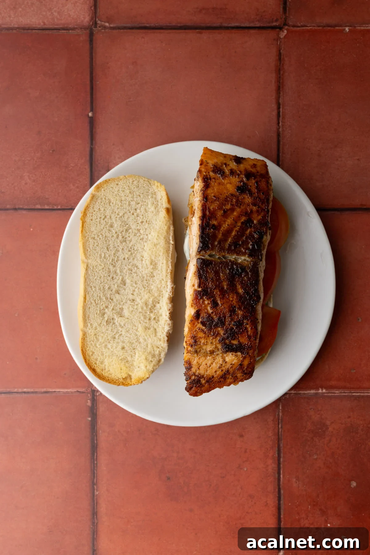 Seared salmon stacked atop sandwich fillings and bread smeared with tartar sauce.