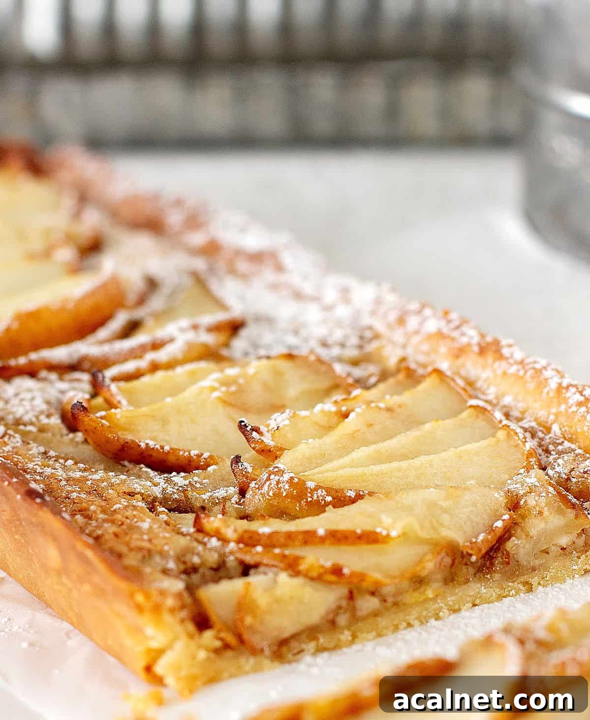 A thin pear tart on white surface with metal pie pans in background