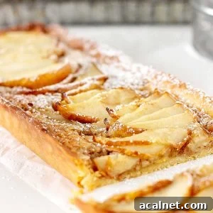 Close up of rectangular pear tart on a white surface with metal pan in the background.