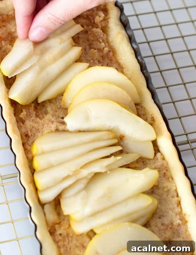 Adding pear slices by hand to long almond tart on a golden wire rack.
