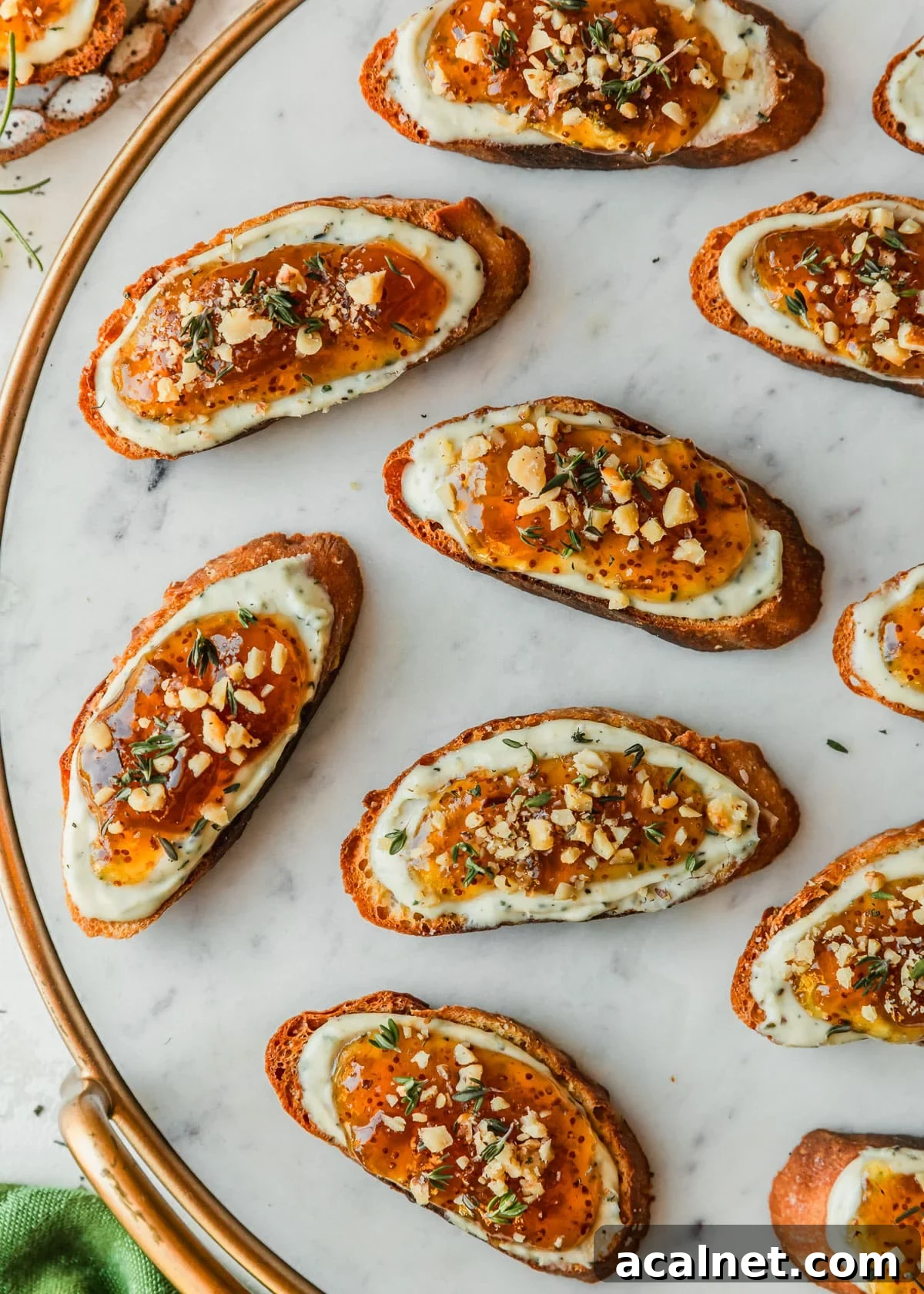 Goat cheese crostini with fig jam, walnuts, & thyme on a white marble board next to a green linen and stoneware plate.